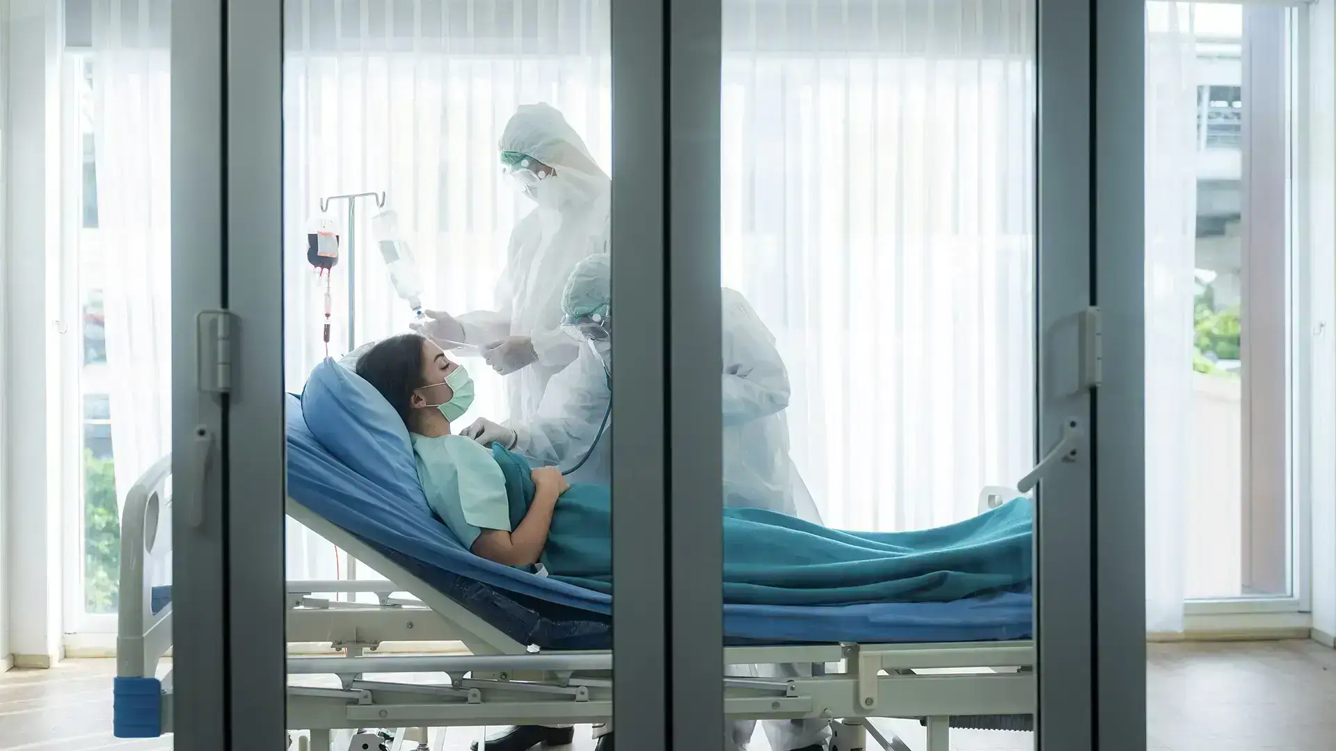 Hospital ICU room with transparent glass doors for patient monitoring.